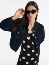 a lady in a denim crop jacket with a black polka dot dress